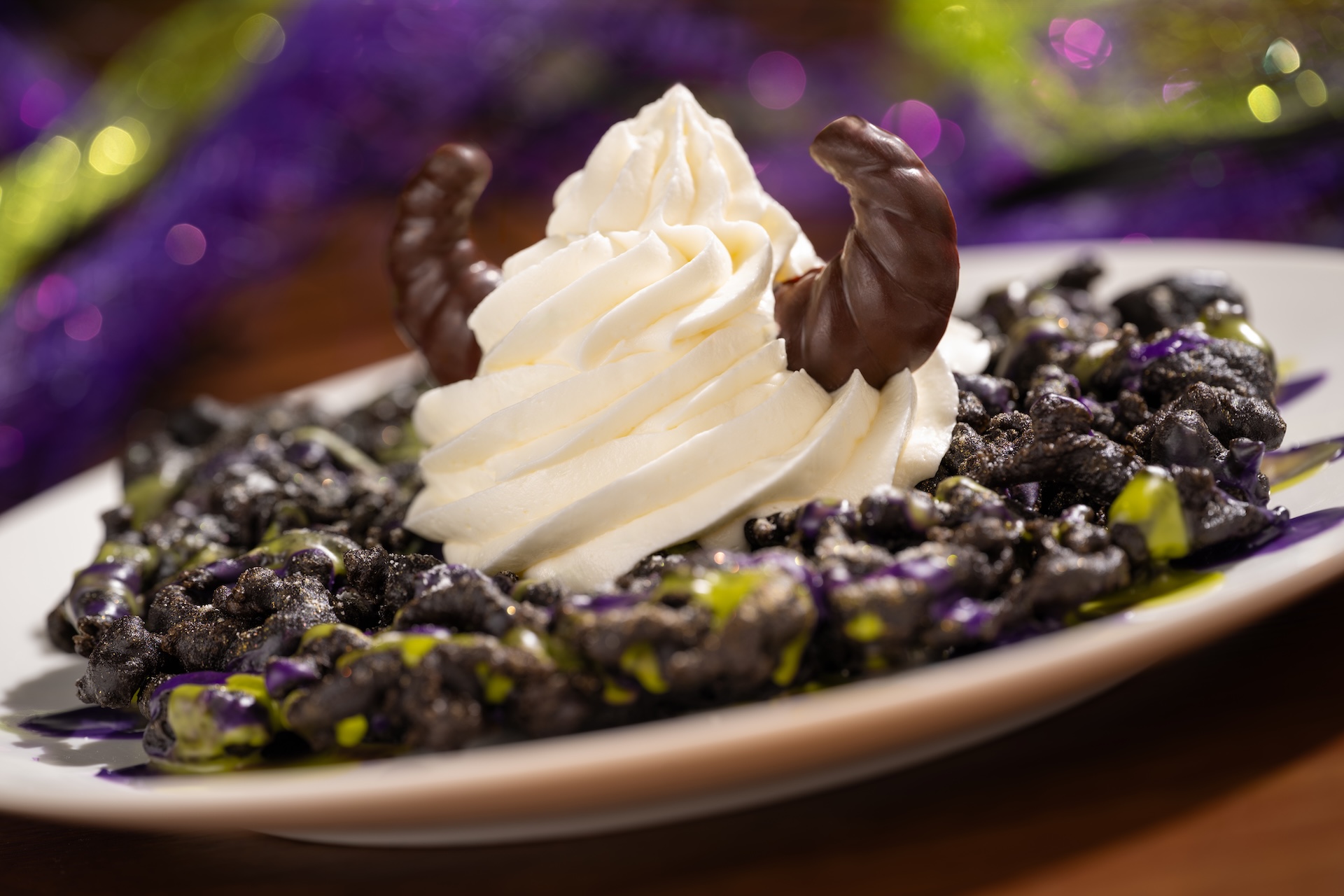 Maleficent Funnel Cake: Chocolate funnel cake topped with shimmer, powdered sugar, ube and matcha icings, vanilla soft-serve, and chocolate horns (New) 
