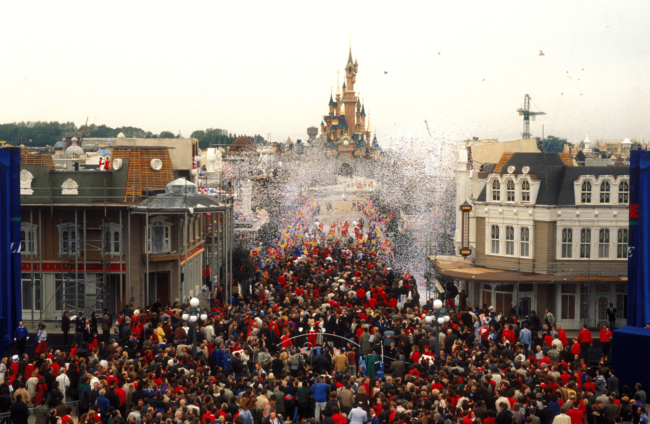 A dense crowd on Main Street, U.S.A. under falling confetti, with Mickey at the centre and the castle in the background.