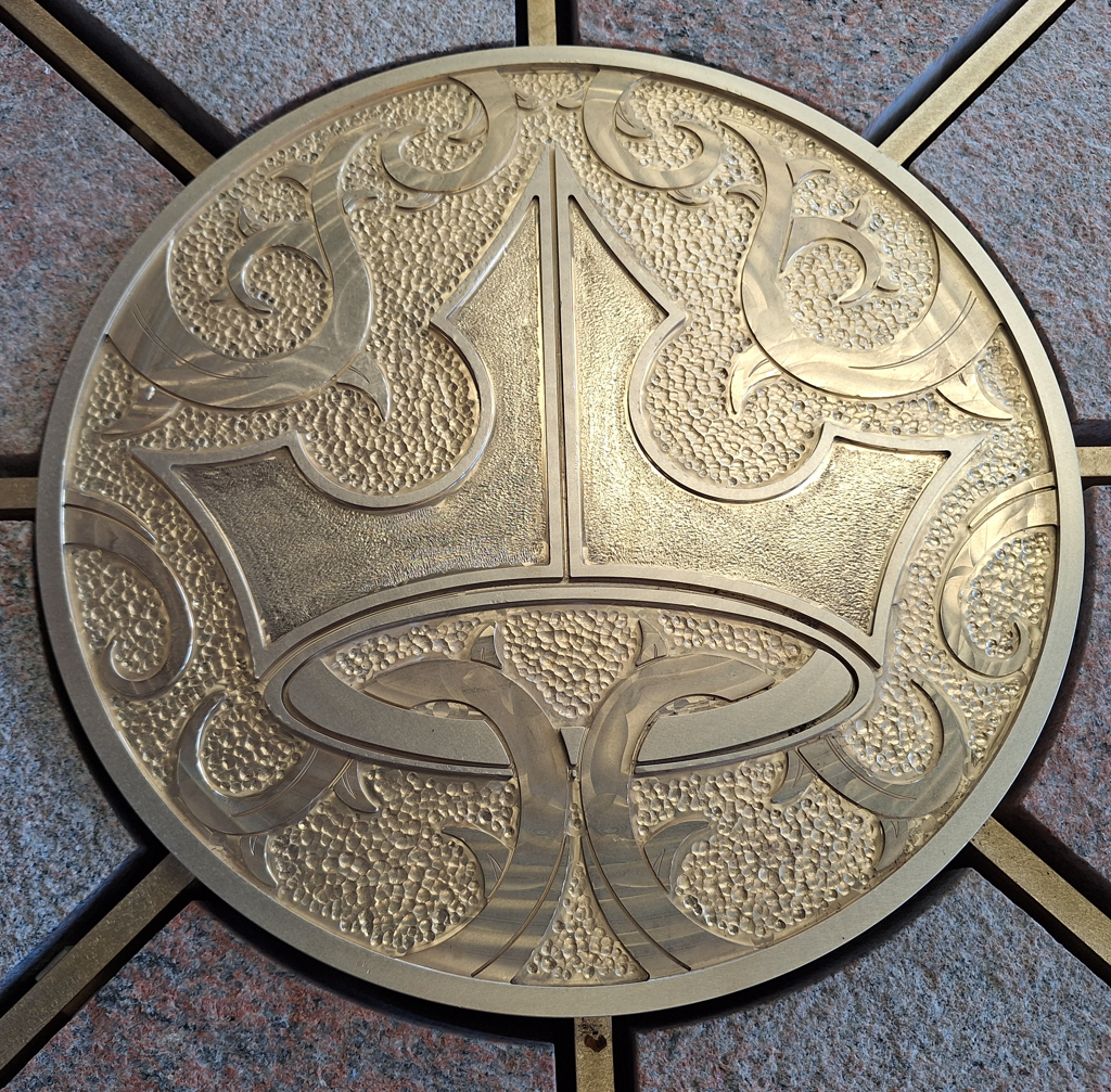 Circular brass medallion with a crown and thorns motifs, hammered and engraved, at the centre of granite rays.